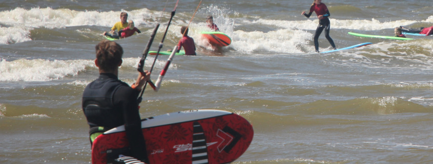 Man loopt met foil het water in tussen de surfers bij Surfschool Castricum. Voorrangs Regels Kitesurfen.