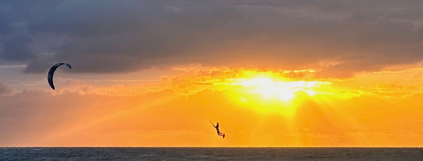 Een kitesurfer maakt een mooie sprongen met een gouden lucht op de achtergrond bij Surfschool Castricum.